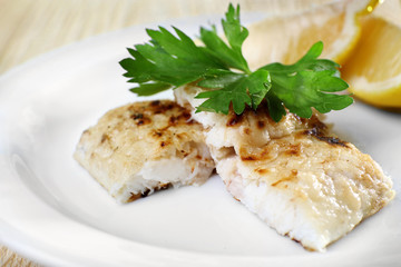 Dish of fish fillet with greens and lemon on plate close up