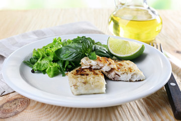 Dish of fish fillet with greens and lime on table close up