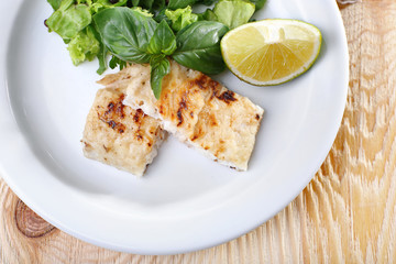 Dish of fish fillet with greens and lime on plate close up