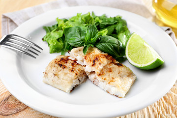 Dish of fish fillet with greens and lime on plate close up