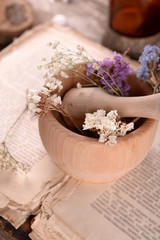 Old book with dry flowers in mortar and bottles on table close up