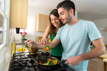 Wall murals Cooking Young attractive couple preparing dinner on a date saving money by cooking at home