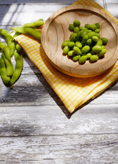 Vertical shot of green soybeans on a wooden plate below the sunlight rays
