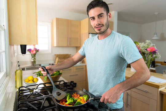 An attractive male uses spatula to turn cooked veggies in frying pan low calorie diet