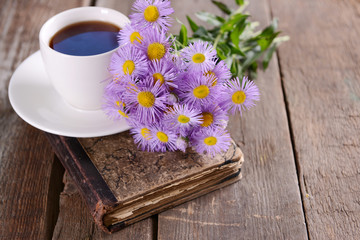 Old book with beautiful flowers and cup of tea on wooden table close up