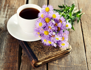 Old book with beautiful flowers and cup of tea on wooden table close up