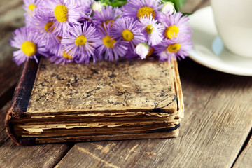 Old book with beautiful flowers and cup of tea on wooden table close up