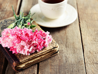 Old book with beautiful flowers and cup of tea on wooden table close up