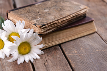 Old books with beautiful flowers on wooden table close up