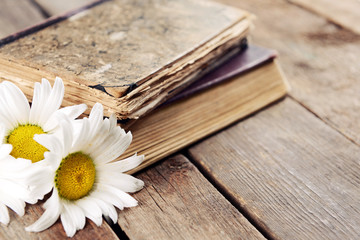 Old books with beautiful flowers on wooden table close up