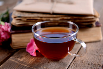 Old books with beautiful flowers and cup of tea on wooden table close up