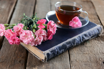 Old book with beautiful flowers and cup of tea on wooden table close up