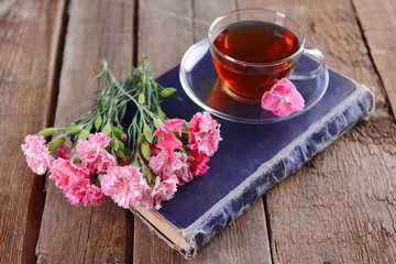 Old book with beautiful flowers and cup of tea on wooden table close up