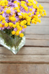 Beautiful small wild flowers in vase on wooden background