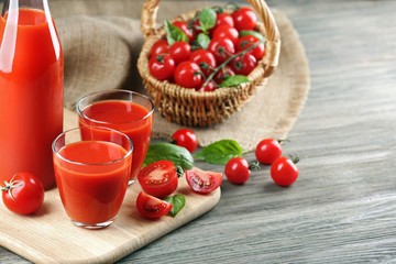 Full bottle and glasses of tomato juice with vegetables on wooden table close up