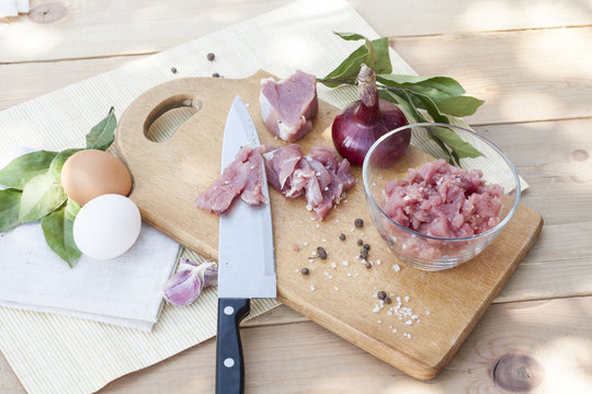 Raw chopped pork tenderloin with herbs in a glass bowl on a wooden board, selective focus