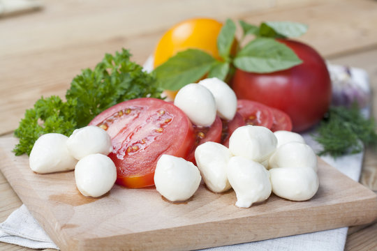 Sliced tomatoes, basil and mozzarella cheese on a wooden board, selective focus