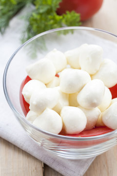 Mozzarella cheese in a glass bowl, tomatoes, sliced tomatoes and herbs on a wooden table, selective focus