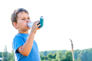 Boy using inhaler for asthma in village with summer sunset