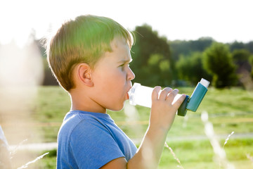 Boy using inhaler for asthma in village with summer sunset - obrazy, fototapety, plakaty