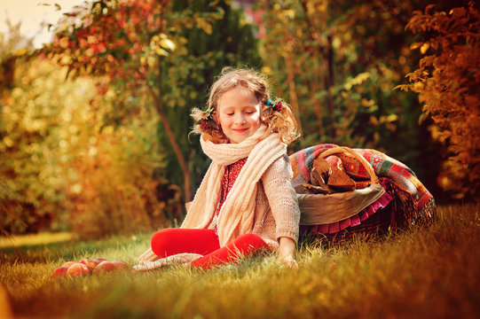 happy child girl sitting with apples in autumn garden