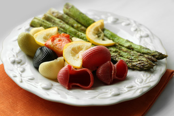 Roasted asparagus and tasty colorful pasta with vegetables on plate on wooden table background