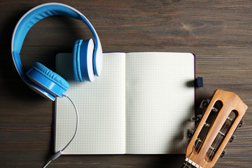 Music recording scene with classical guitar, notebook and headphones on wooden table, closeup