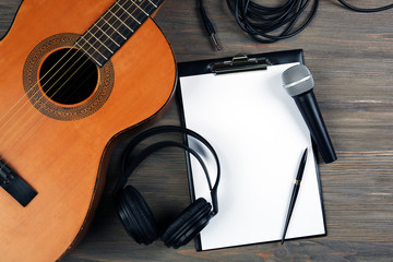 Music recording scene with classical guitar, headphones, microphone and memo pad on wooden table,...