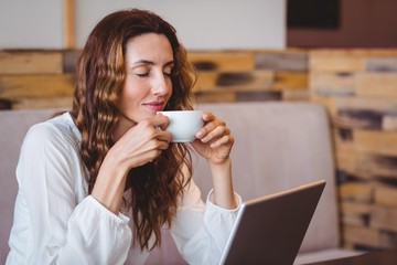 Pretty brunette having coffee using laptop