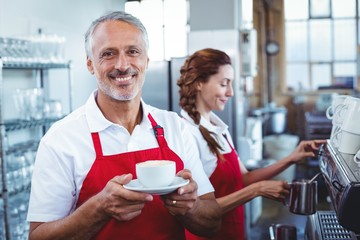 Happy barista smiling at camera and holding a cup of coffee