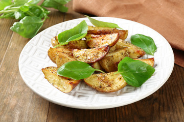 Baked potatoes with basil leaves in white plate on wooden table, closeup