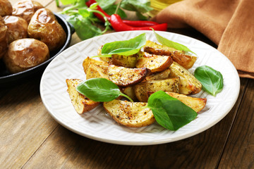 Baked potatoes with basil leaves in white plate on wooden table, closeup