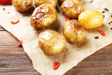Baked spicy potatoes on parchment on wooden table, closeup