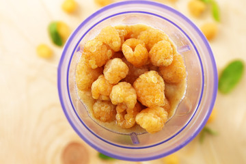 Yellow raspberries in blender cup on wooden table, closeup