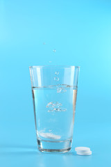 Glass of water and pills on blue background