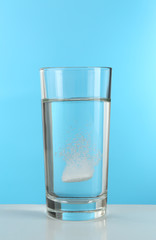 Pill in glass of water on blue background