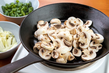 Sliced champignon mushrooms on cast iron skillet , ready to cook mushroom sauce