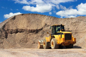 Bulldozer in sand and gravel site with cloudy blue sky