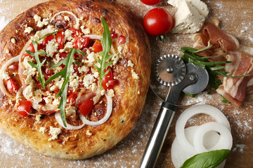 Greek homemade pizza with ham,onion, roasted tomato, creamy feta on wooden table background