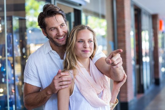 Smiling man embracing his girlfriend and pointing far away