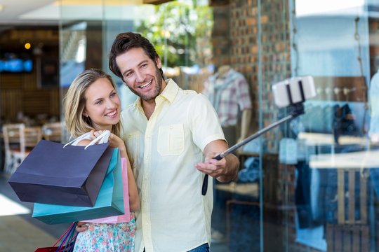 Smiling couple with shopping bags taking selfies with selfiestick
