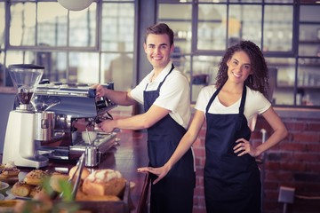 Smiling waitress in front of colleague making coffee