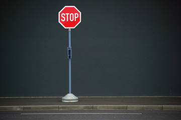 Stopschild / Ein Stopschild steht vor einer homogenen Wand am Gehweg