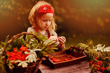 happy child girl making rowan berry beads in sunny autumn garden - obrazy, fototapety, plakaty