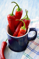 Red chili peppers in blue cup on blue wooden background