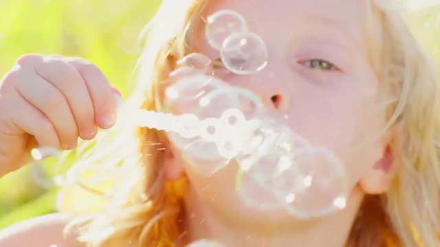 Young blonde girl blowing bubbles outside