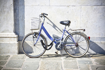 Old blue women bicycle with basket against a marble wall