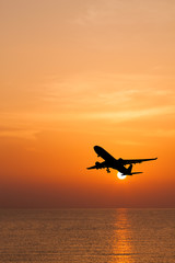 Silhouetted commercial airplane flying above the sea at sunset