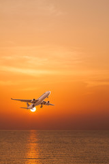 Fototapeta na wymiar Commercial airplane flying above the sea at sunset