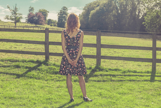 Young woman standing in field by fence on summer day